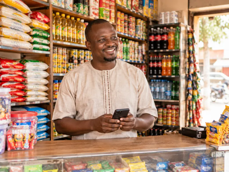 Le gérant d'une épicerie de quartier, téléphone en main, derrière son comptoir